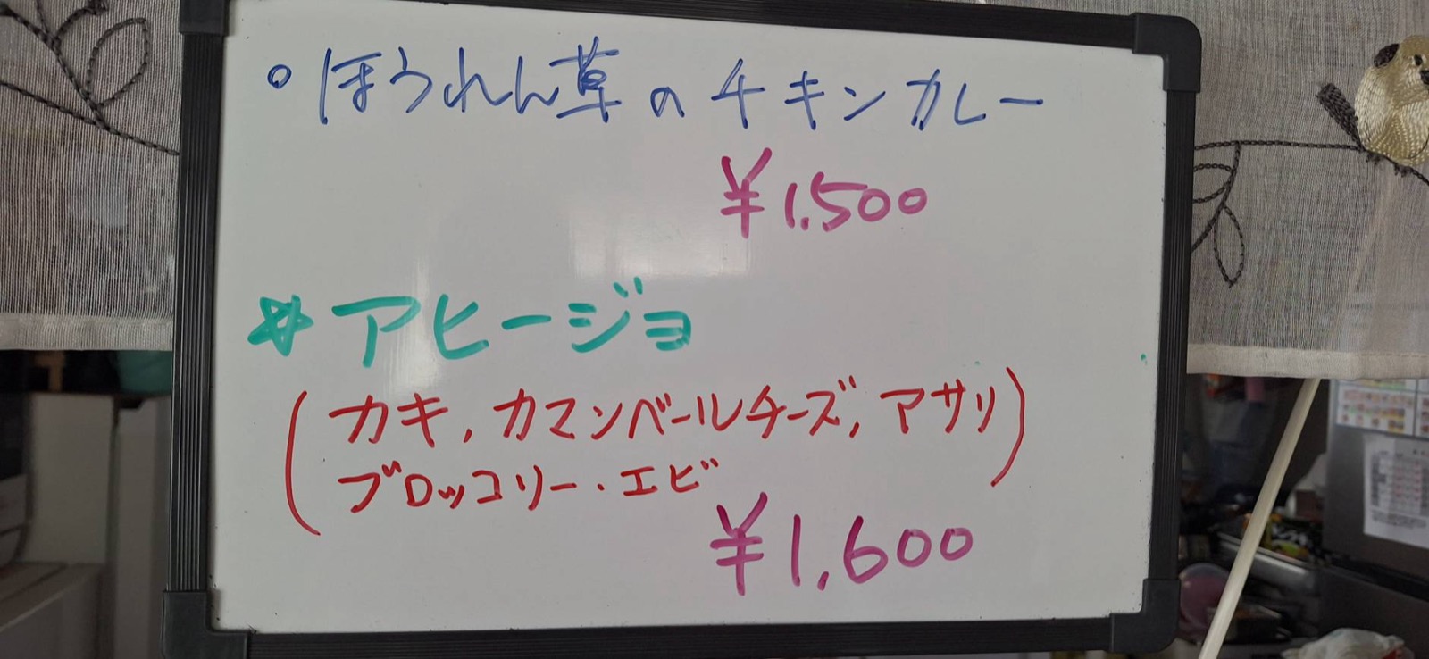 ホワイトボードに書かれたほうれん草のチキンカレーとアヒージョのメニュー