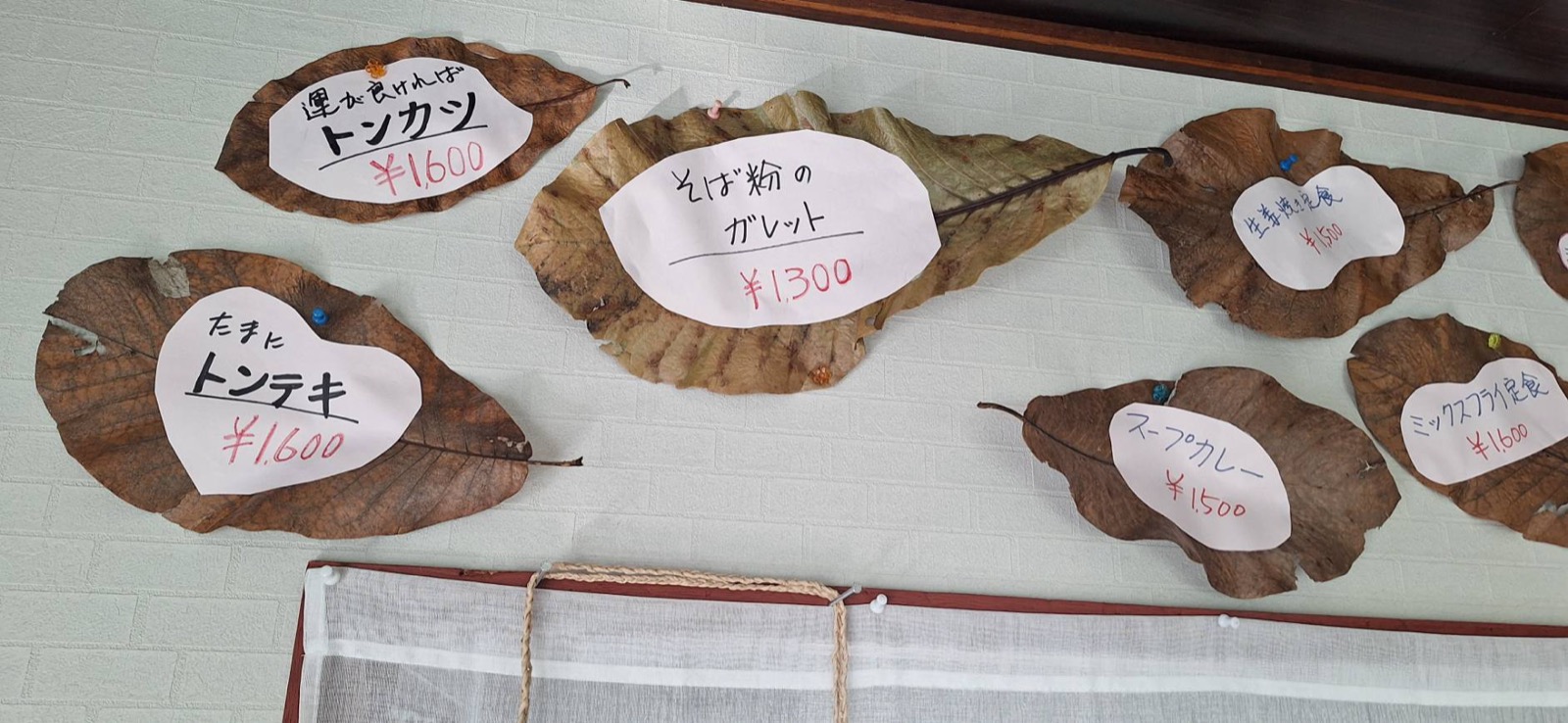 朴葉に書かれたトンカツ・トンテキ・そば粉のガレットなどのメニューが壁に貼られている