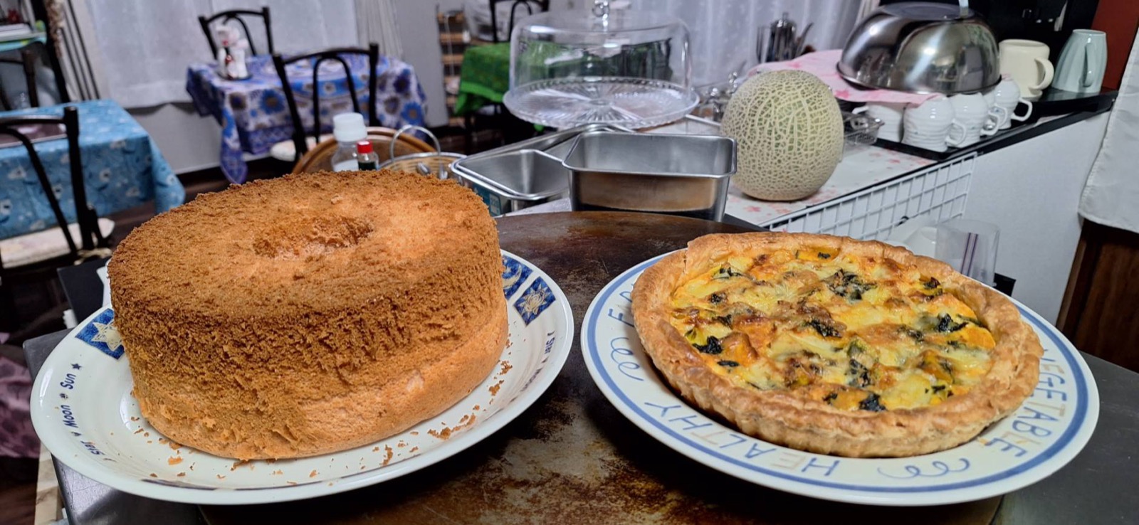 夜の厨房で焼き上がった丸いケーキとキッシュが並んでいる様子