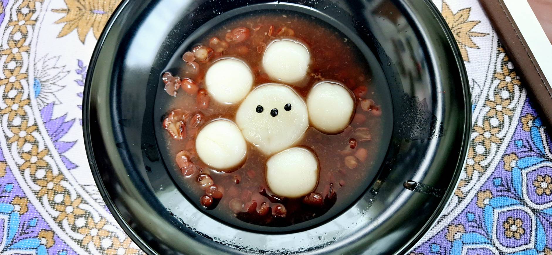 黒いお皿に盛り付けた白玉ぜんざい。中央の白玉がシマエナガのような顔になっている