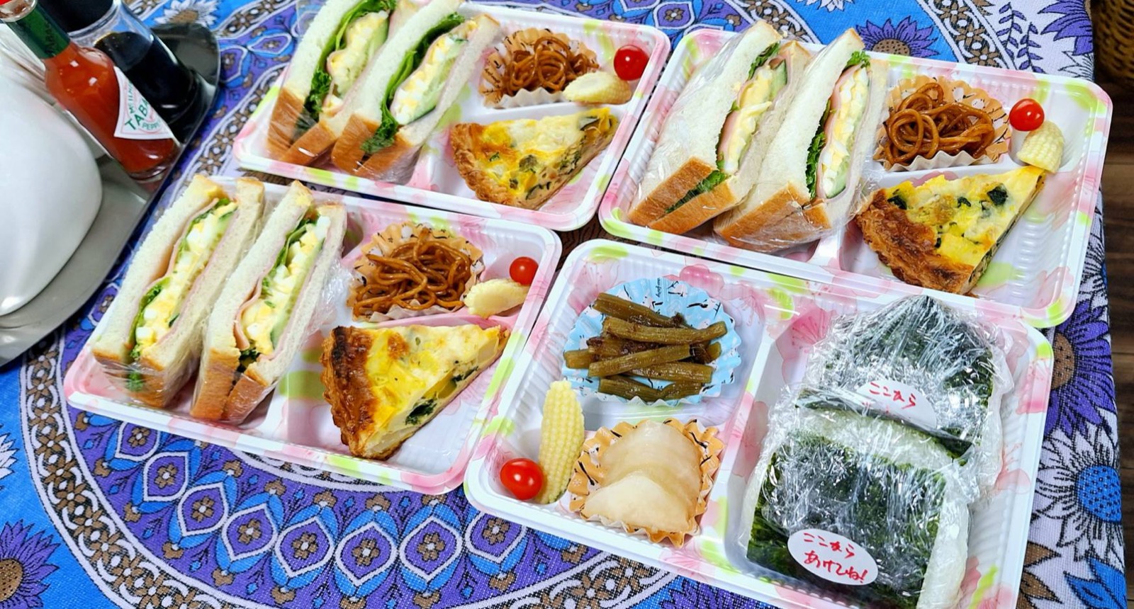 キッシュと卵サンドイッチのセット3つと、のり付きおにぎりセットが並んだテイクアウト弁当